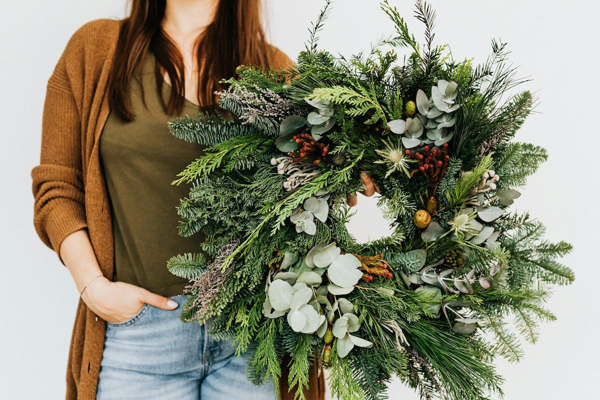 Wreath Making Workshop at The Hive in Newburyport Massachusetts. Woman holding holiday wreath with fresh greens, berries, and pinecones