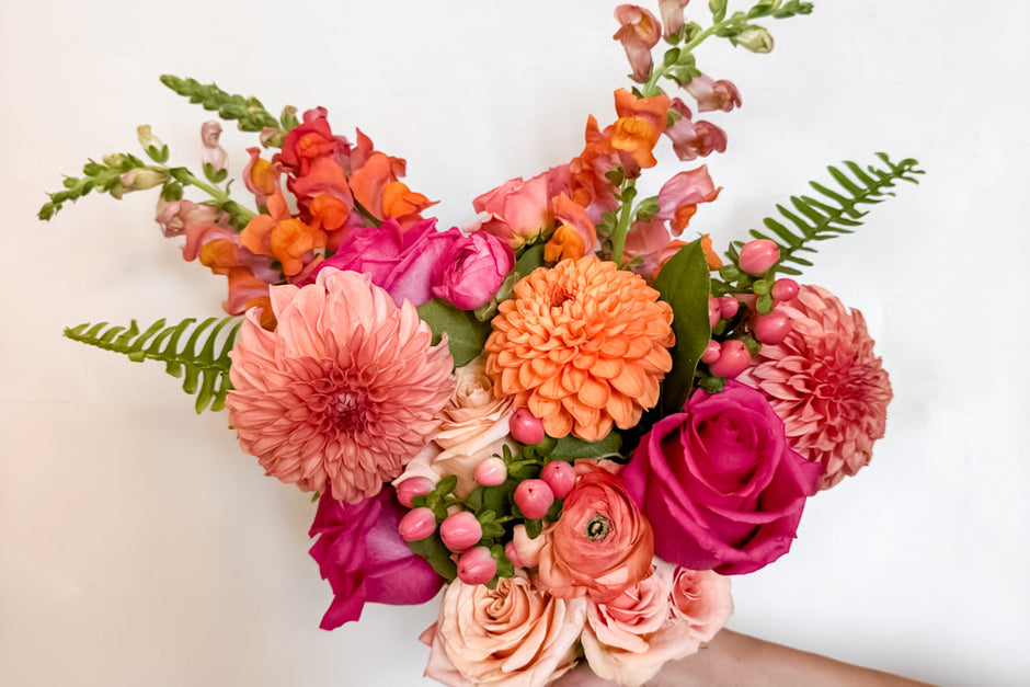 Bouquet of colorful flowers held by a hand on a light background